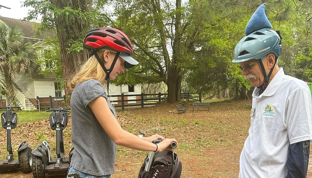 A young woman and an older man with quirky helmets are preparing for a Segway ride outdoors