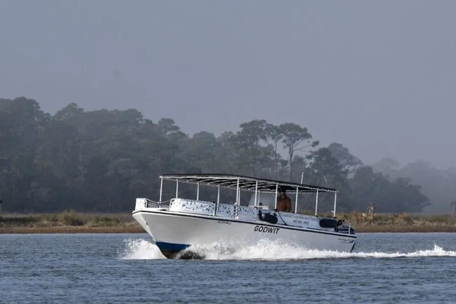 A motorboat named GODWIT is cruising through the water, making a wake, with a person visible at the helm.