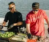 Two chefs are grilling an assortment of fresh vegetables and meats on a boat