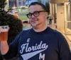 A man in glasses and a Florida sweatshirt is smiling while holding a cup of beer outdoors