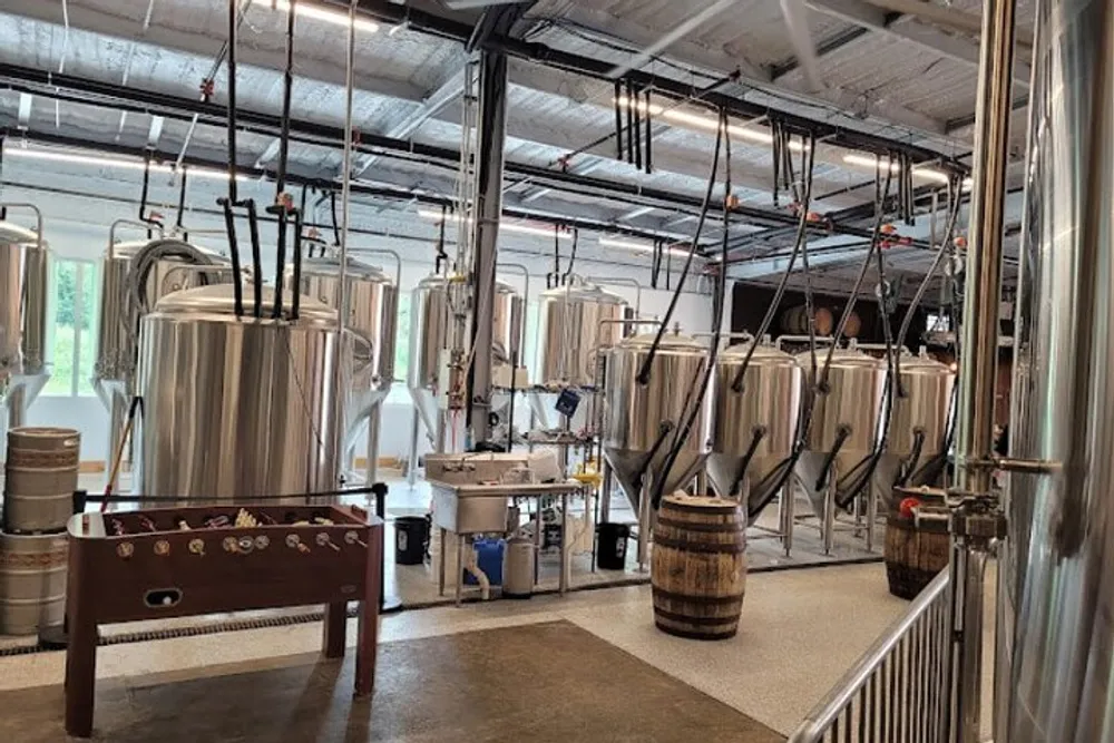 The image shows the interior of a brewery with stainless steel fermentation tanks and brewing equipment
