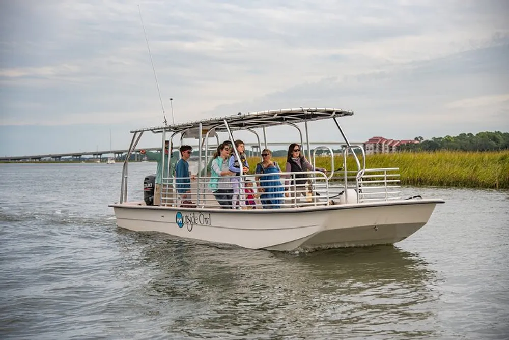 A group of people are enjoying a boat ride on a calm river with lush greenery on one side and a cloudy sky above