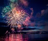 A vibrant fireworks display lights up the night sky above a body of water reflecting colorful bursts on its surface