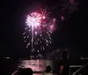 A vibrant fireworks display lights up the night sky above a body of water reflecting colorful bursts on its surface
