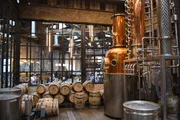The image shows an interior view of a distillery with copper stills and aging barrels, highlighting the production process of spirits such as whiskey.