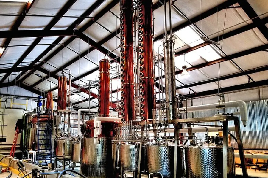 The image shows a distillery equipped with copper distillation columns and stainless steel tanks, indicative of spirits production.