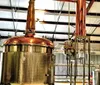 The image shows an interior view of a distillery with copper stills and aging barrels highlighting the production process of spirits such as whiskey