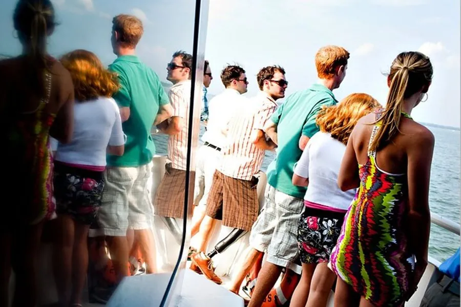 A group of casually dressed people are standing on a boat, looking out over the water.
