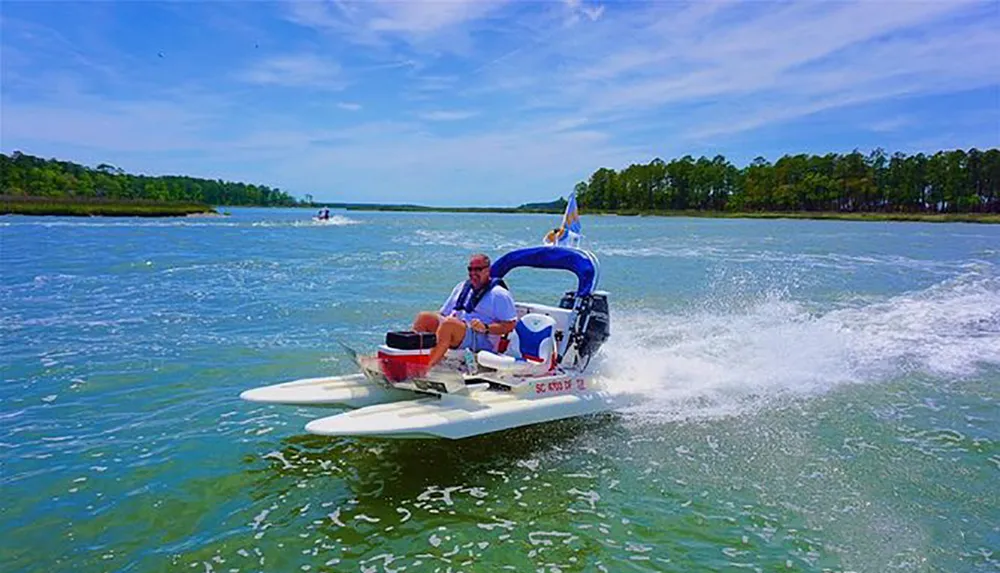 A person is riding a compact motorized watercraft across a body of water with trees and other boats in the background