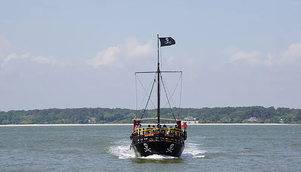 A boat designed to resemble a pirate ship is sailing on the water with a Jolly Roger flag flying atop its mast