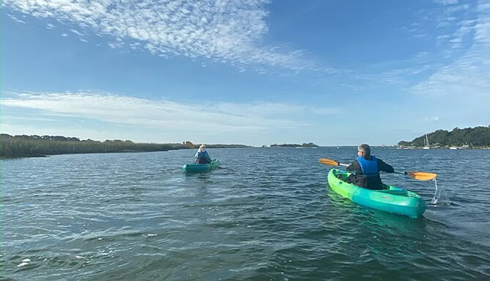 Two individuals are kayaking on a calm body of water under a partly cloudy sky