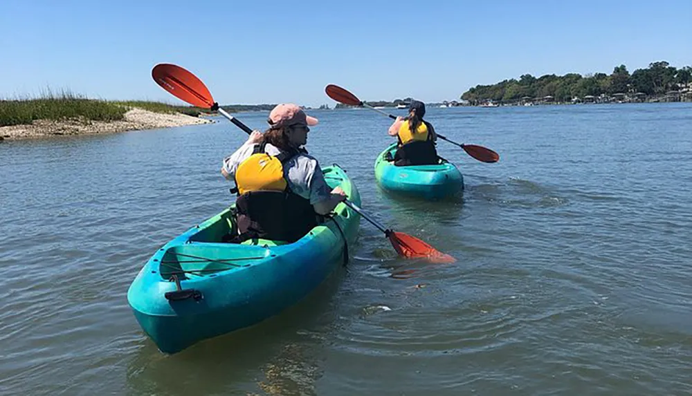 Two people in life vests are kayaking on calm water on a sunny day