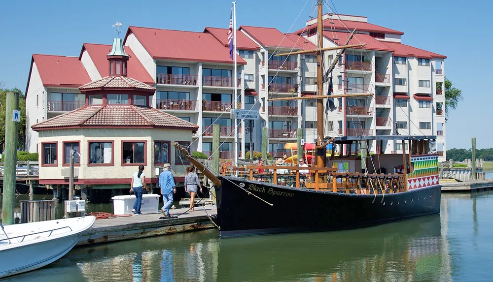 A pirate-themed ship named Black Sparrow is docked near a multi-story waterfront building with people walking along the dock
