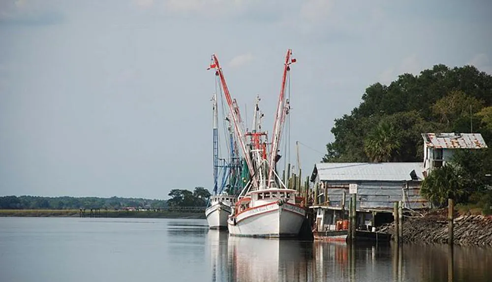 The image shows fishing boats moored at a rustic dock along a calm river reflecting a serene maritime scene