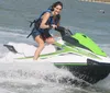 A smiling person is riding a jet ski at high speed over water