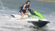 A smiling person is riding a jet ski at high speed over water.