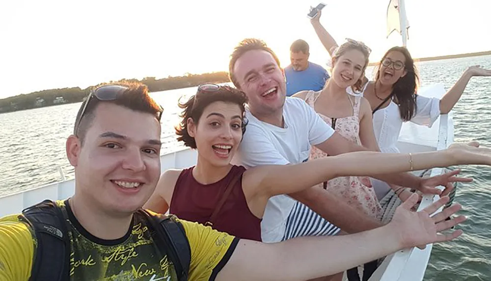 A group of friends is taking a joyful selfie on a boat enjoying a scenic sunset out on the water