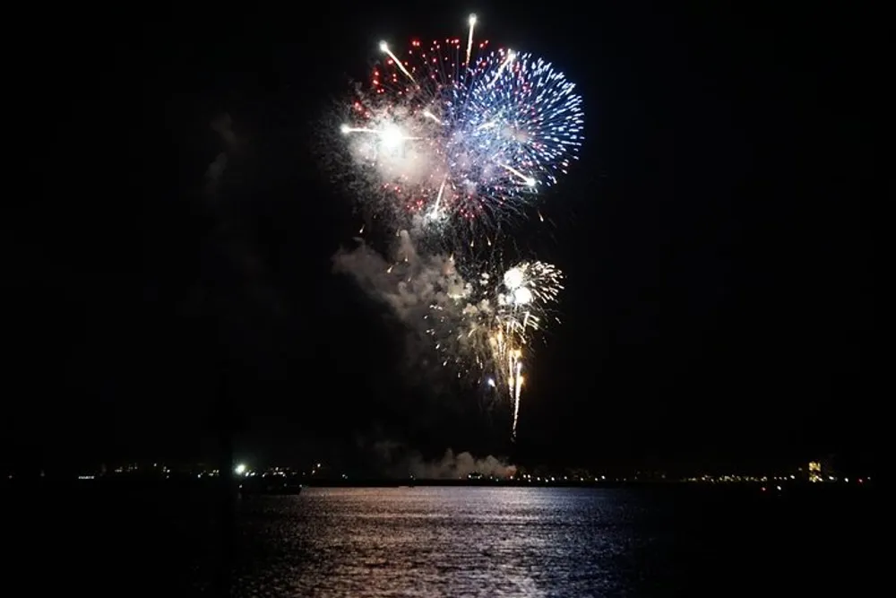 The image displays a vibrant display of fireworks bursting over a body of water at night