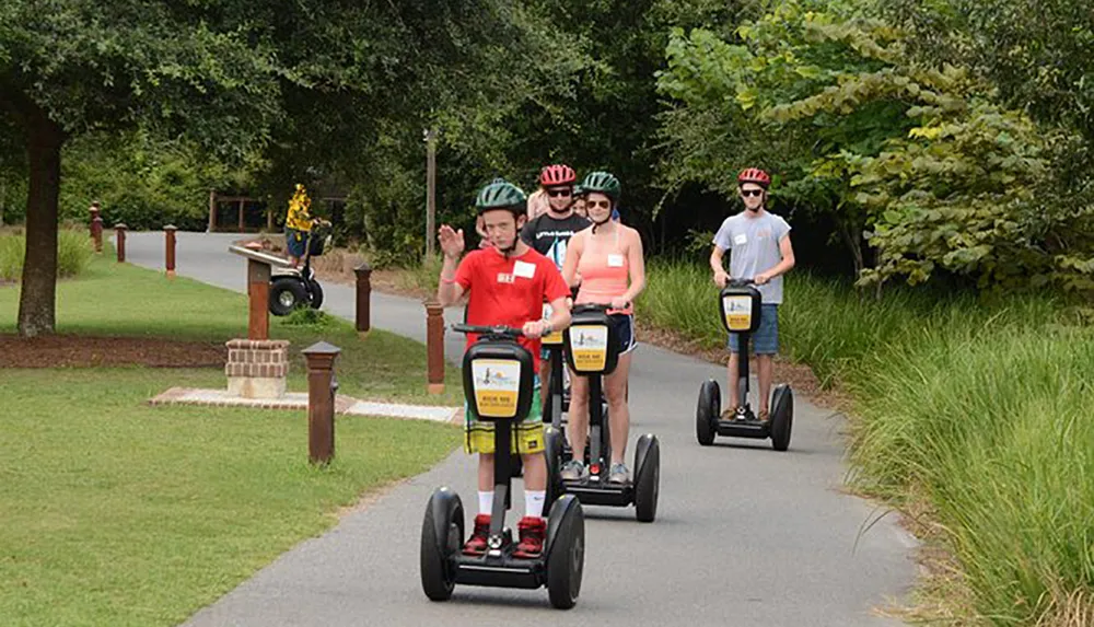 A group of people wearing helmets ride Segways in single file along a park path