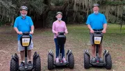 Three people, each wearing a helmet, are standing outdoors with their individual Segways, smiling for the camera.