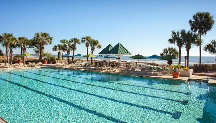 A serene outdoor swimming pool area with sun loungers and umbrellas overlooking a calm sea under a clear blue sky