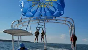 Two people are preparing to parasail over the water with a vibrant blue parasail emblazoned with 
