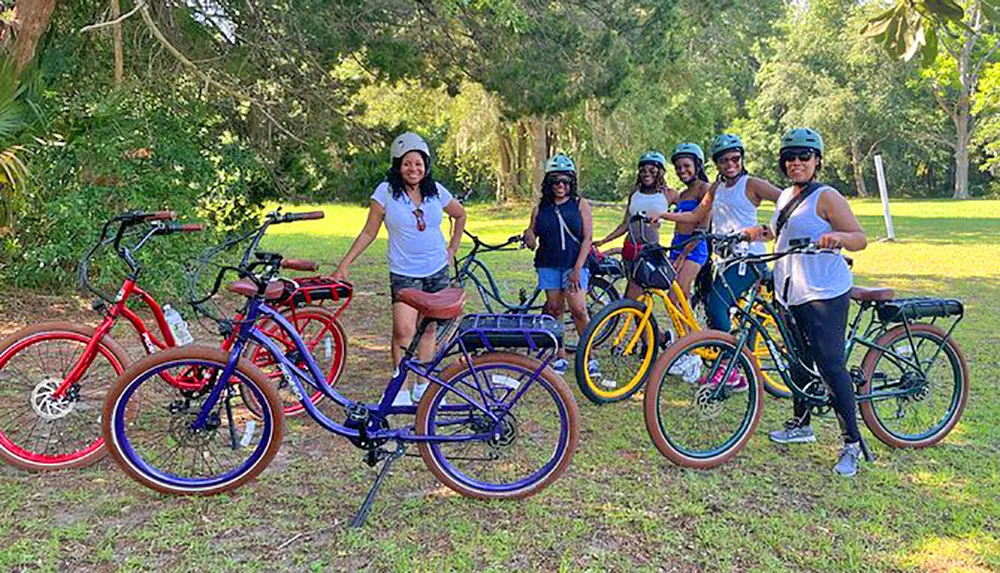 A group of smiling people wearing helmets is standing beside a line of colorful bicycles in a park