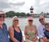 A group of five people are smiling and posing for a photo on a boat with a picturesque lighthouse and waterfront buildings in the background