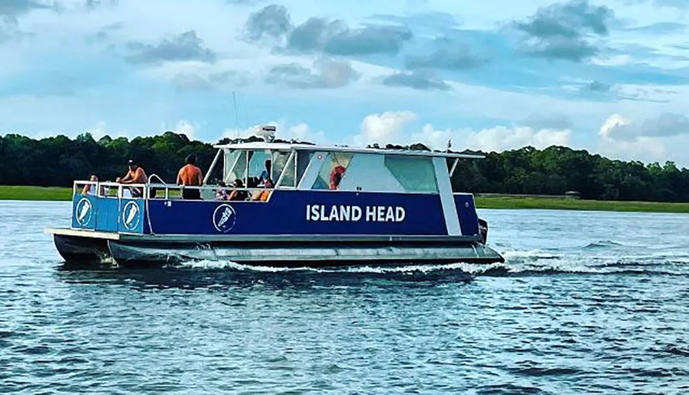 A boat labeled ISLAND HEAD is cruising on the water with several passengers on board set against a backdrop of clouds and distant greenery