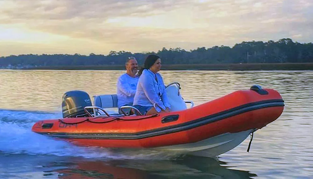 Two people are enjoying a ride on an inflatable boat across calm waters at dusk
