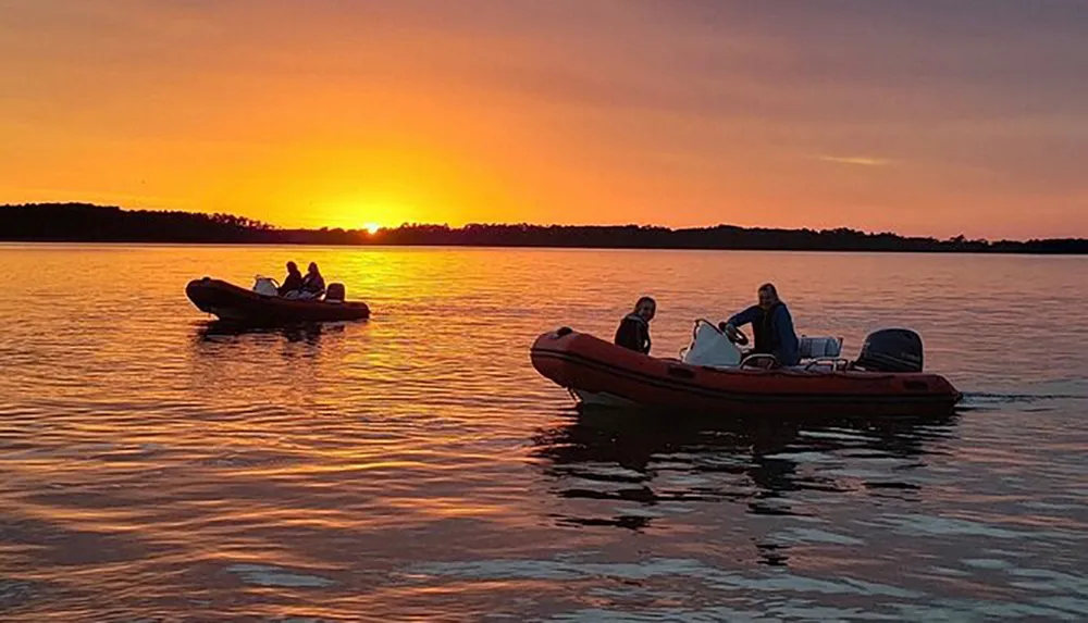 The image shows people on two boats enjoying a stunning sunset over calm waters