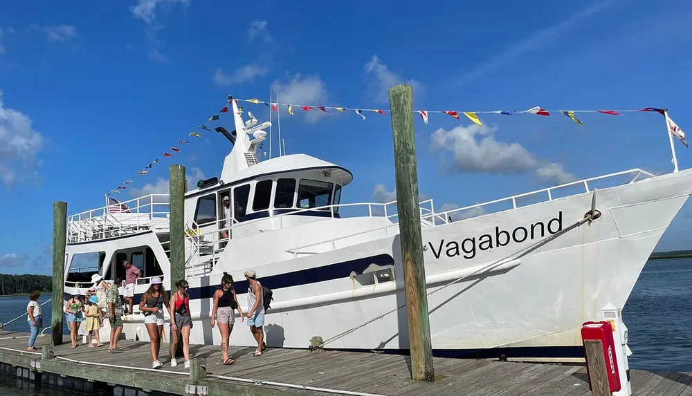 Passengers are disembarking from a white boat named Vagabond onto a wooden dock under a clear blue sky