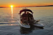 Two individuals are enjoying a peaceful moment on a pedal boat at sunset on a calm water body.