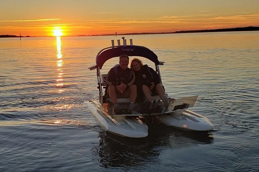 Two individuals are enjoying a peaceful moment on a pedal boat at sunset on a calm water body.