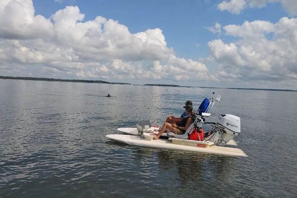 A person is seated on a motorized watercraft appearing relaxed on a calm lake with a clear sky above and land visible on the horizon