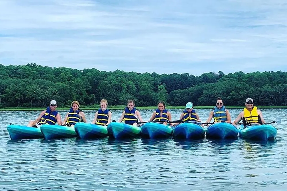 Eight individuals in life jackets are enjoying a group kayaking experience on a calm water body