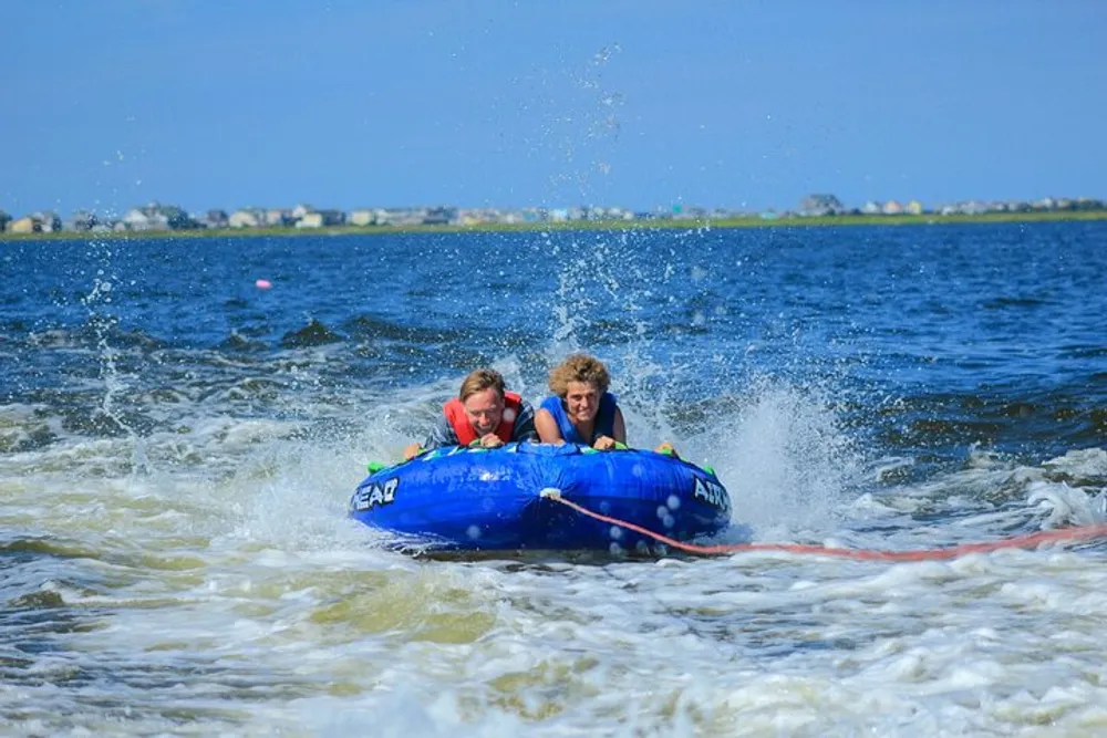 Two people are enjoying a thrilling ride on a water tube being towed across a lake with splashing water all around them