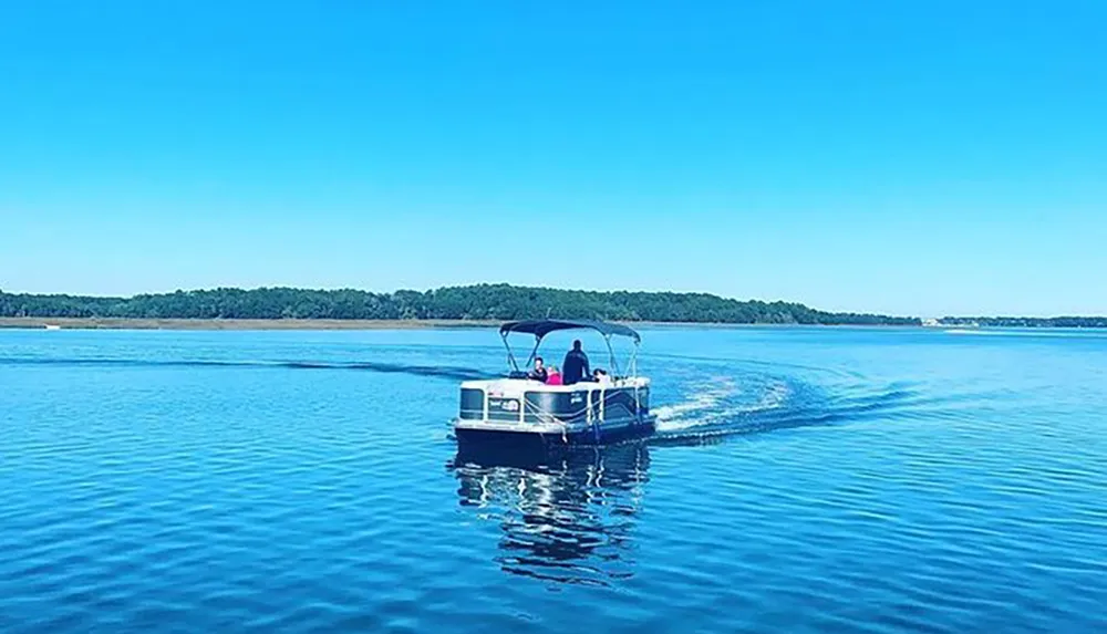 A pontoon boat is cruising on a calm blue lake under a clear sky
