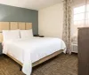 This image depicts a tidy and modern hotel room with a neatly made bed a nightstand with a lamp a patterned curtain and a dresser with a television