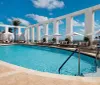 The image shows a serene resort swimming pool flanked by white columns and loungers under a clear blue sky