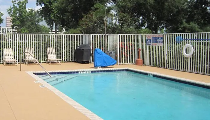 An outdoor swimming pool is surrounded by a metal fence with lounge chairs a grill covered with a tarp and a life ring mounted on the fence