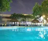 An illuminated swimming pool area in the evening surrounded by tropical trees and lounging facilities reflects the tranquil ambiance of a resort-like setting