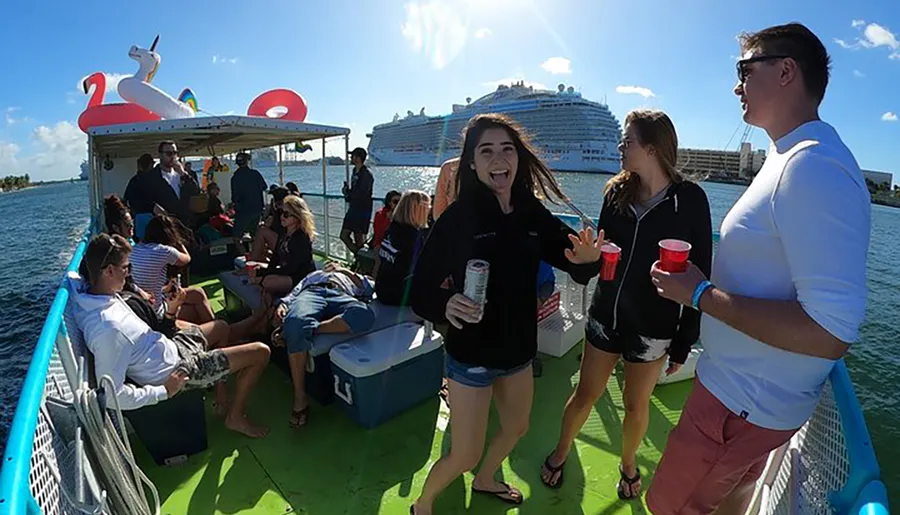A group of people is enjoying a sunny day on a floating platform with inflatables and beverages, with a large cruise ship in the background.