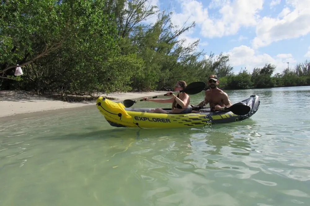 Two people are kayaking near the shore in clear shallow water