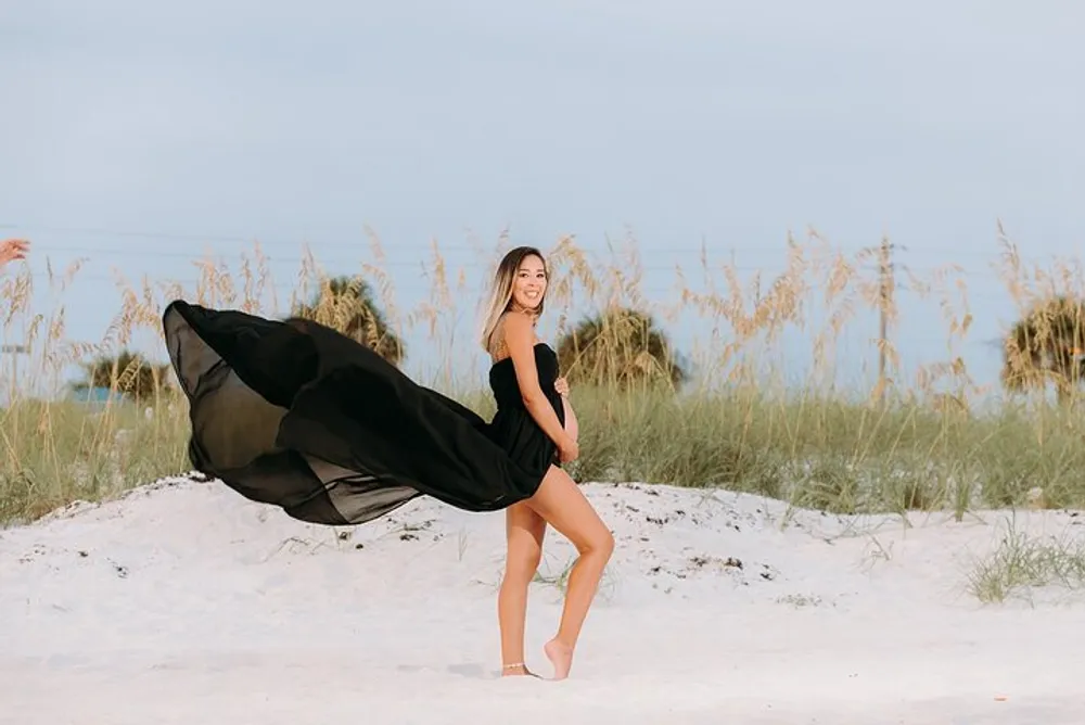 A person in a black outfit is posing on a beach with a fabric trailing behind evoking a sense of motion and elegance