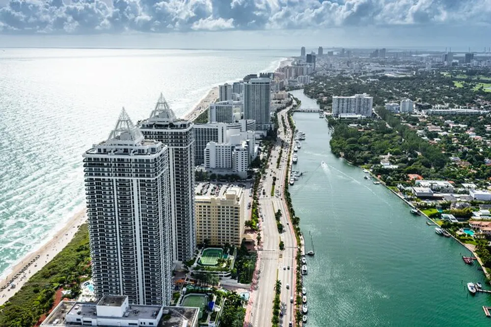 This aerial image captures the scenic coastline of a bustling city with towering skyscrapers adjacent to a sunlit beach and a calm waterway