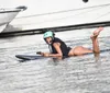 A person is riding a hydrofoil board near luxurious yachts in a sunny marina setting