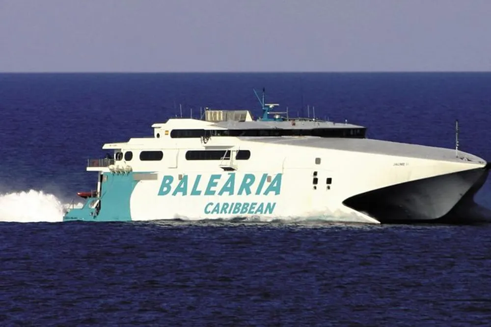 A white and blue high-speed ferry labeled BALEARIA CARIBBEAN is cruising on the open sea