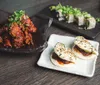 The image features an assortment of Asian cuisine dishes including spicy glazed chicken steamed buns and sushi rolls on a wooden table