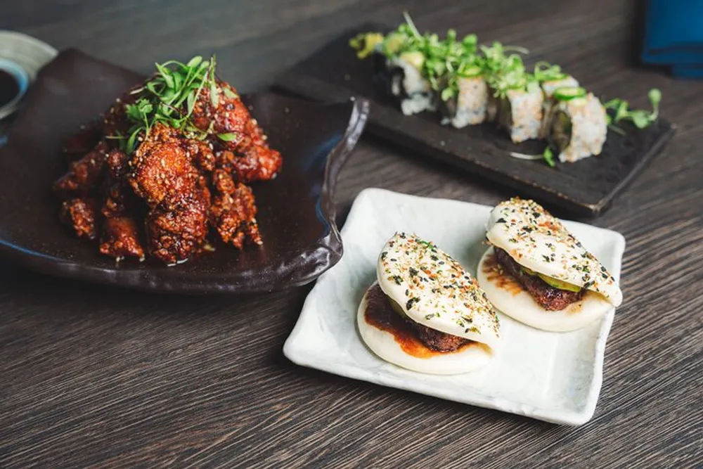 The image features an assortment of Asian cuisine dishes including spicy glazed chicken steamed buns and sushi rolls on a wooden table